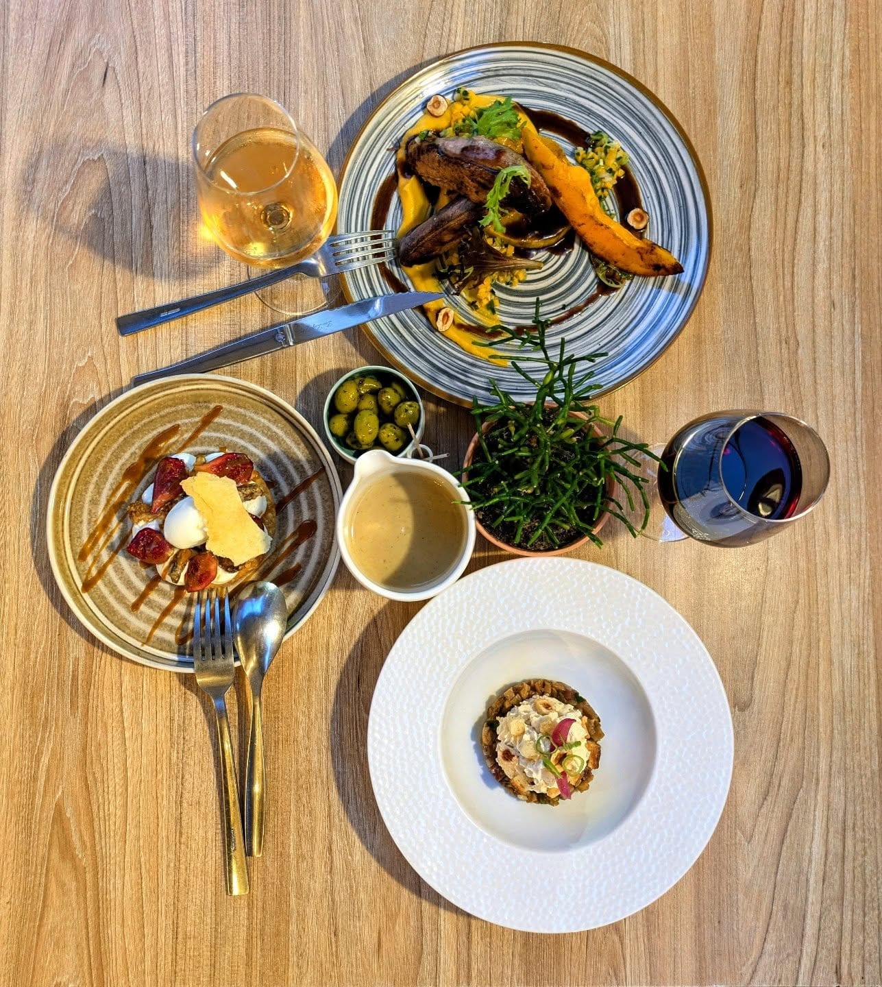 Table dressée en terrasse au Pèbre d'Aï : assiettes de saison, verre de vin et lumière du soir